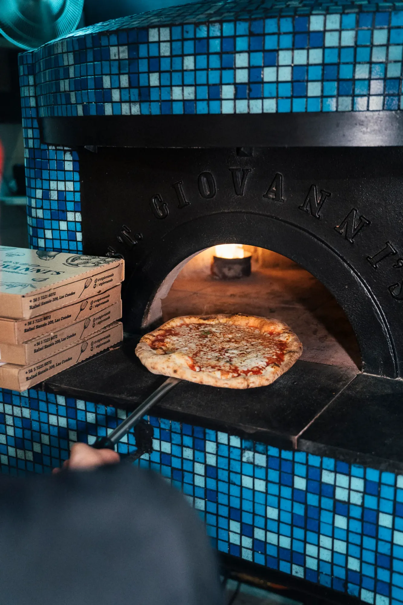 Horno de barro artesanal de St. Giovanni's sacando una pizza margherita, con cajas del local de Rafael Sanzio